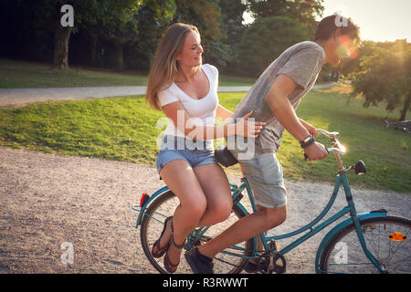 Junges Paar Reiten Fahrrad im Park, Frau sitzt auf der Zahnstange Stockfoto