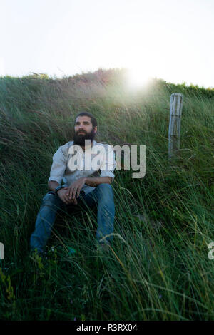 Junge Mann sitzt auf Gras in den Dünen, Tagträumen Stockfoto