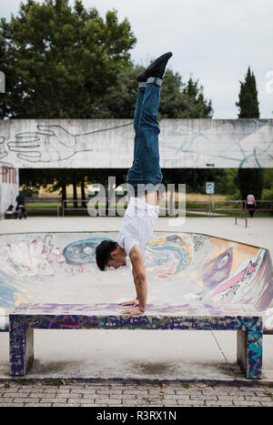 Junger Mann macht einen Handstand auf der Werkbank im Skatepark Stockfoto