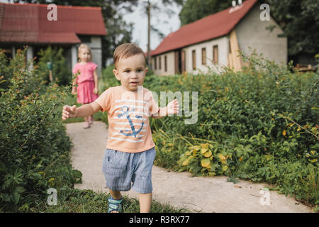 Baby Boy walking in Garten mit Schwester im Hintergrund Stockfoto