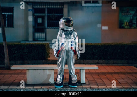 Spaceman stehend auf einer Bank in der Stadt bei Nacht Stockfoto