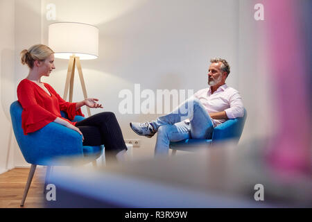 Reifer Mann und junge Frau sitzt im Sessel sprechen Stockfoto