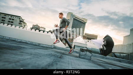 Mann tun Trainings mit Widerstand Fallschirm auf dem Dach. Seitenansicht eines Fitness Mann laufen mit einem Widerstand Fallschirm auf der Terrasse eines Gebäudes. Stockfoto