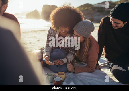 Zwei junge Frau Entspannen am Meer mit Handy. Gruppe von Freunden am Strand sitzen Sie ihr Smartphone. Stockfoto