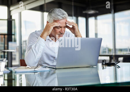 Betonte Geschäftsmann am Schreibtisch mit Laptop sitzen, den Kopf Holding Stockfoto