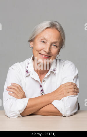 Portrait der älteren Frau mit grauen Haaren sitzen am Tisch Stockfoto