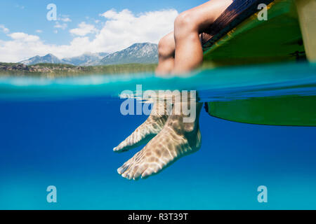Füße von Ein Junge sitzt auf dem Boot im Wasser baumelt. Stockfoto