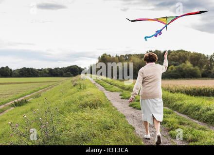 Ältere Frau zu Fuß mit Kite in ländlichen Landschaft Stockfoto