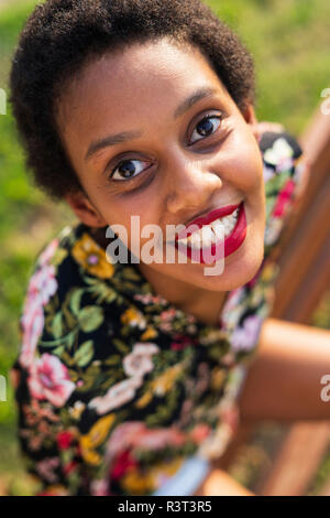 Portrait von lächelnden jungen Frau sitzt auf der Bank im Park