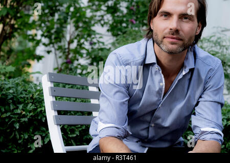 Portrait von zuversichtlich Mann sitzt auf Stuhl im Garten Stockfoto