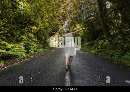 Neuseeland, Nordinsel, Egmont National Park, Frau Balancing auf der Mittellinie auf der Straße Stockfoto