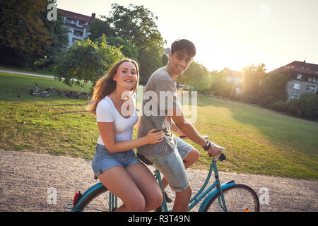 Junges Paar Reiten Fahrrad im Park, Frau sitzt auf der Zahnstange Stockfoto