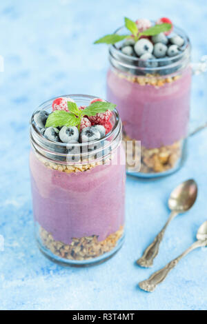 Zwei Gläser Joghurt mit Erdnuss Müsli, aronia Pulver und Nachfüllen von gehackten Haselnüssen und Gefrorene Beeren Stockfoto