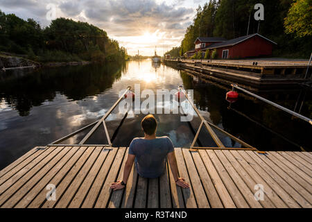 Finnland, Kajaani, Mann sitzt auf Jetty, Sonnenuntergang, Ansicht von hinten Stockfoto