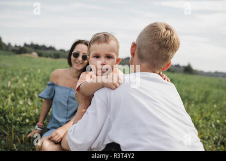 Bruder trösten Baby weinen auf einem Feld mit Mutter im Hintergrund Stockfoto