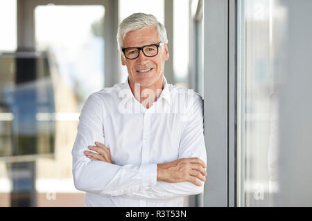 Unternehmer im Amt lehnte sich gegen Fenster, mit gekreuzten Armen Stockfoto