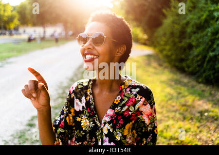 Glückliche junge Frau mit Sonnenbrille im Freien bei Sonnenuntergang Stockfoto