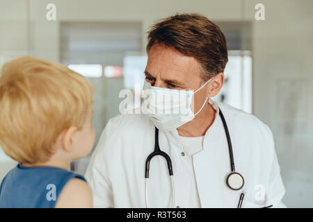 Kind auf den Schoß der Kinderarzt, durch das Tragen von schützender Maske Stockfoto
