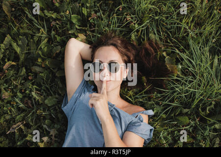 Porträt der lächelnde Frau mit Sonnenbrille im Gras liegend Stockfoto