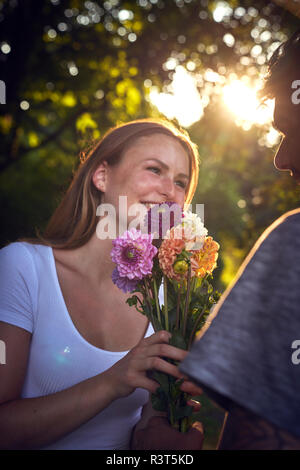 Junger Mann, seine Freundin in einem Park, ihre Geschenke mit Blumen Stockfoto