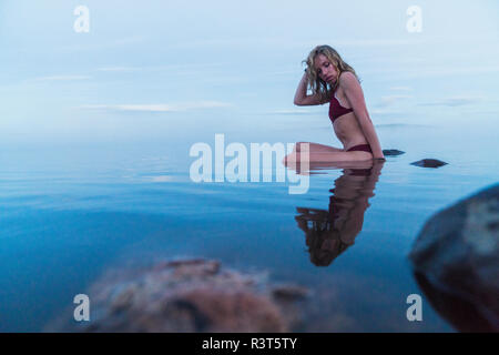Junge Frau, tragen, Bikini, sitzt auf einem Stein in einem See Stockfoto