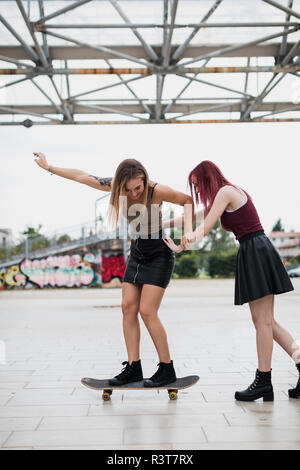 Junge Frau schieben Freund auf Skateboard in der Stadt Stockfoto