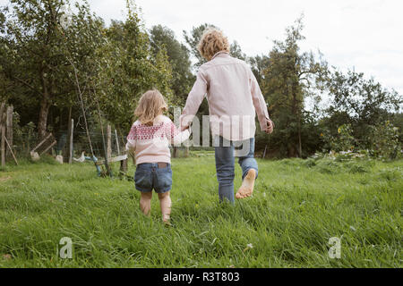 Rückansicht des Bruder und seine kleine Schwester zu Fuß barfoot auf einer Wiese Stockfoto