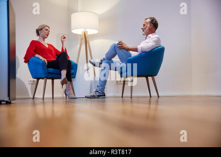 Reifer Mann und junge Frau sitzt im Sessel sprechen Stockfoto