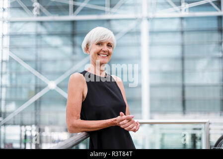 Portrait von lächelnden älteren Frau mit schwarzen Kleid gegen ein Geländer gelehnt Stockfoto