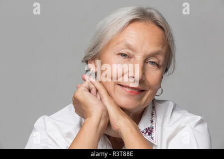 Portrait von entspannt ältere Frau mit grauen Haaren vor grauem Hintergrund Stockfoto