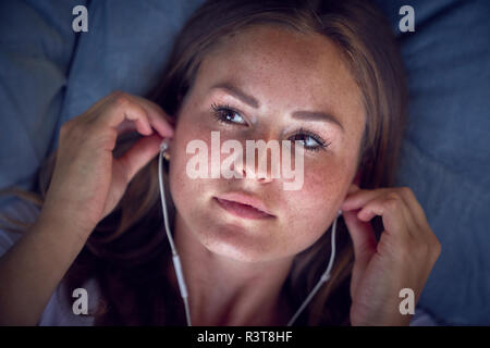 Junge Frau lag auf Kissen, Musik hören mit Kopfhörern Stockfoto