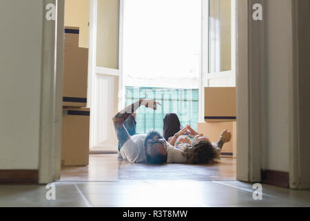 Paar Seite an Seite auf dem Boden der neuen zu Hause vor der geöffneten Balkontür Stockfoto