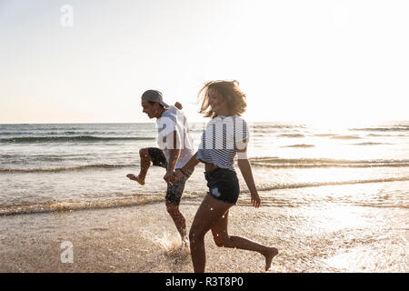Junges Paar, das Spaß am Strand, Spritzwasser in das Meer Stockfoto