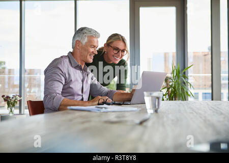 Lächelnd reifes Paar mit Laptop auf dem Tisch zu Hause Stockfoto