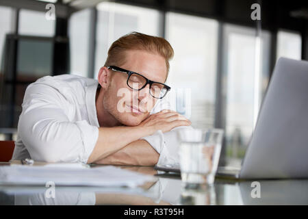 Unternehmer lehnen auf Schreibtisch im Büro mit geschlossenen Augen Stockfoto