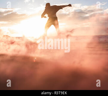 Mann tut Bewegung Training am Strand mit bunten Rauch bei Sonnenuntergang Stockfoto