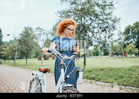 Junge Frau wandern im Park, Fahrrad schieben Stockfoto