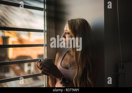 Blonde junge Frau mit kaffeebecher Blick aus Fenster Stockfoto