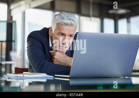 Geschäftsmann am Schreibtisch sitzen und versuchen, ein Problem zu lösen Stockfoto