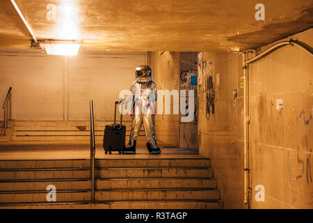 Spaceman in der Stadt in der Nacht stehend in Unterführung mit rollenden Koffer und Kaffee zum Mitnehmen Stockfoto