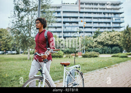 Junger Mann mit Rucksack Fahrrad drücken in Park Stockfoto