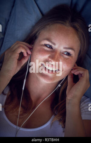 Junge Frau lag auf Kissen, Musik hören mit Kopfhörern Stockfoto