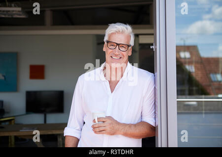 Portrait von lächelnden reifer Mann mit Tasse Kaffee auf dem Balkon zu Hause Stockfoto