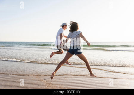 Ein junges Paar, das Spaß am Strand, Laufen und Springen am Meer Stockfoto