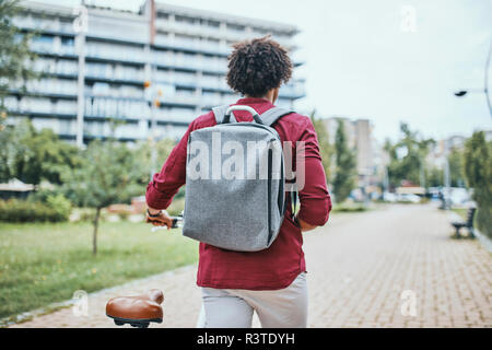 Junger Mann mit Rucksack Fahrrad drücken in Park Stockfoto