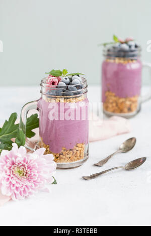 Zwei Gläser Joghurt mit Erdnuss Müsli, aronia Pulver und Nachfüllen von gehackten Haselnüssen und Gefrorene Beeren Stockfoto
