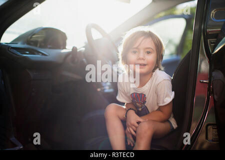 Portrait von kleiner Junge sitzt auf dem Fahrersitz im Auto an der Hintergrundbeleuchtung Stockfoto