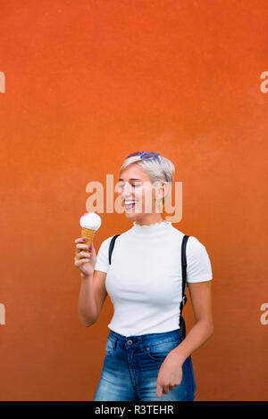 Lachende junge Frau mit Eis vor orangen Hintergrund Stockfoto