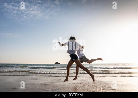 Ein junges Paar, das Spaß am Strand, Laufen und Springen am Meer Stockfoto