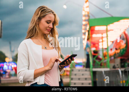 Junge Frau mit Handy auf einem Jahrmarkt Stockfoto